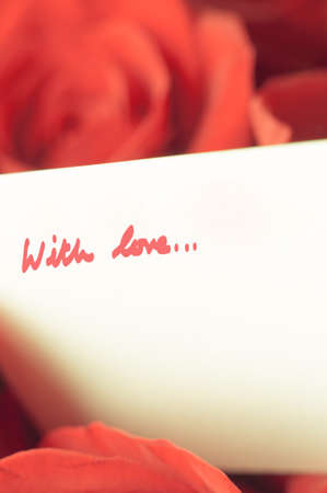 Soft focus roses in faded coral red hues with white message card and words 'With love' attached.  Retro appearance.の写真素材