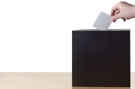 Hand placing folded voting slip into slot in ballot box on light wood table.  Isolated on white background.の写真素材