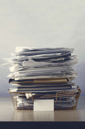A wire office tray with blank label, piled up with papers and folders, undersaturated in drab hues for dreary, dystopian feel.の写真素材