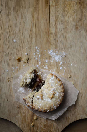 Overhead shot of a partially eaten Christmas mince pie with crumbling pastry and dusting of icing sugar, on an old wooden chopping board.の写真素材