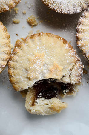 Overhead close up of one mince pie in a group, broken open as if partially eaten.  White Icing sugar sprinkles on pastry and surface.の写真素材