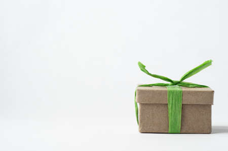 Eye level shot of simple brown gift box in lower right of frame with closed lid, tied with light green raffia ribbon on off white background.の写真素材