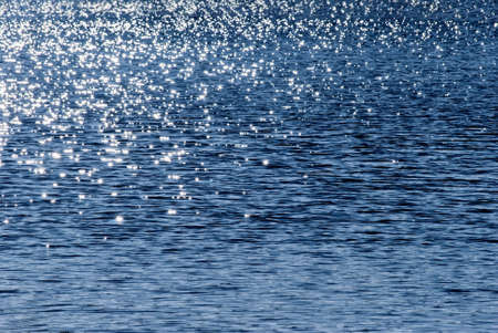 Water texture.  Deep blue, gently rippled sea water filling frame with bright, sparkling dappled sunlight.の写真素材