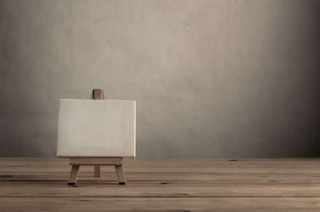 Blank art canvas on easel standing to left of frame on wood plank floor with empty wall behind and to the right.の写真素材