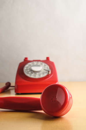 Eye level shot of a retro red 1960s to 70s British style telephone, with receiver off the hook and in close up foreground.  Dial base in soft focus background.の写真素材