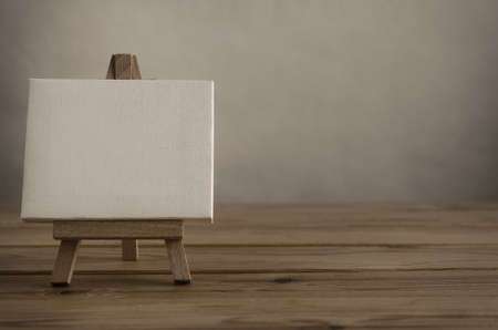 Close Shot of blank art canvas on easel standing to left of frame on wood plank floor as if in gallery or studio with empty wall behind and to the right.の写真素材