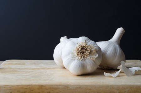Three whole garlic bulbs on old light wood chopping board with scattered peelings. Black chalkboard background.の写真素材