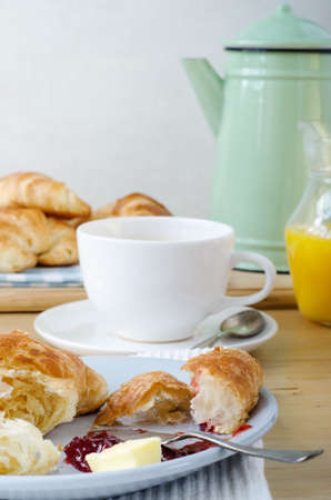 Continental Breakfast table setting laid with croissants, orange juice and coffee. A serving of partly eaten croissant with butter and jam is in the foreground.の写真素材