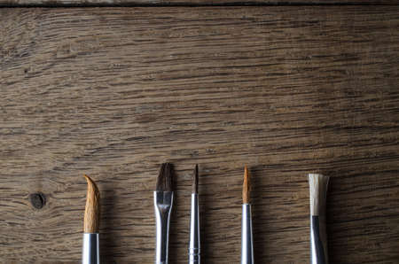Overhead shot of five artist's paintbrushes, lined up in a row and pointing up into copyspace on an Oak wood table.の写真素材