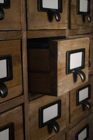 Angled side view of card index drawers lit by a bright light in a dark room. One drawer opened.の写真素材