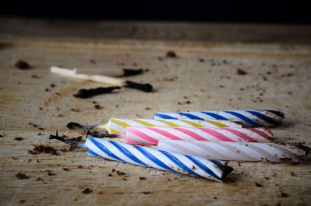 Used birthday candles and matches, burned and blackened. Left scattered on a wooden chopping board with cake crumbs as remnants at the end of party celebrations.の写真素材