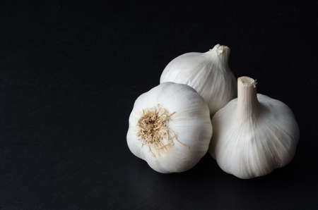 Angled, elevated shot of three whole garlic bulbs on black slate with copy space to the left.の写真素材