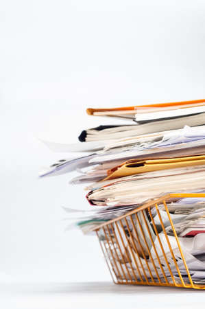 Angled shot of a yellow wire office filing or in tray, stacked high with a messy pile of documents. Copy space on white background to left and above.の写真素材