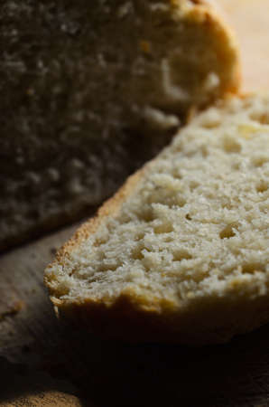 Freshly baked loaf of bread, with first slice cut and lying face up on wooden chopping board with...