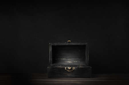 A dark wooden treasure chest with lid open and lit on planked surface with black chalkboard background.の写真素材