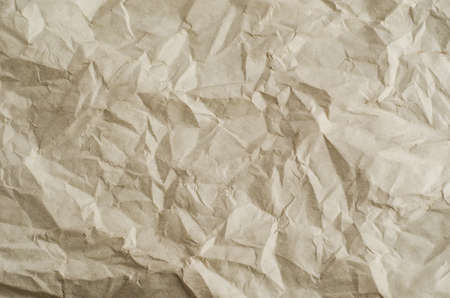 Crumpled, creased and unfolded paper background texture in a neutral parchment hue.の写真素材