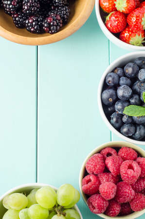 Overhead shot of five fruit varieties in separate bowls bordering frame edge of aqua blue wood planked table.の写真素材