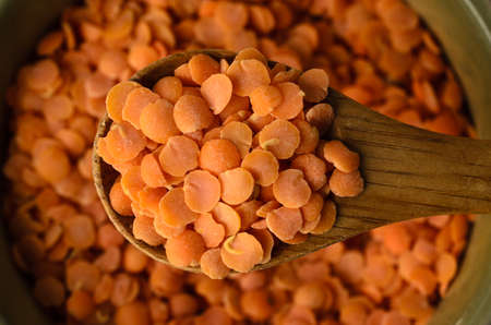 Overhead close up (macro) of a wooden spoon filled with red lentils and lifted towards viewer.  Full...
