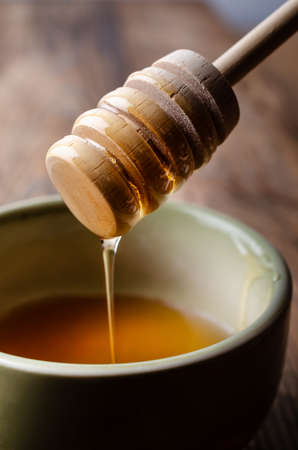 A coated wooden drizzler, lifting and dripping clear, golden honey over a green ceramic, partly...