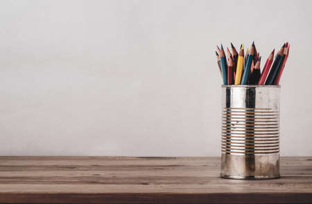 A variety of coloured pencils in an old metal tin on a wood plank desk with copy space to left and above. Filtered for retro effect.の写真素材