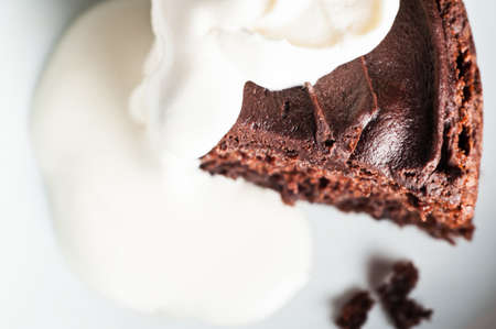 Overhead shot of a slice of iced brown chocolate sponge cake, partly covered in thick cream which...