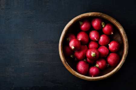 Overhead shot of radishes filling an old wooden bowl on grungy black surface with copy space to the left.の写真素材