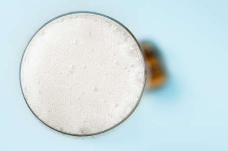 Overhead close up of a champagne glass, filled to the top and frothing with white bubbles.  Cork rests on pale blue table in soft focus background.の写真素材