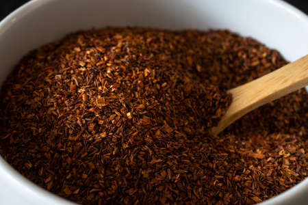Close up shot of dried Rooibos (Redbush) tea leaves in a white ceramic bowl with wooden spoon.