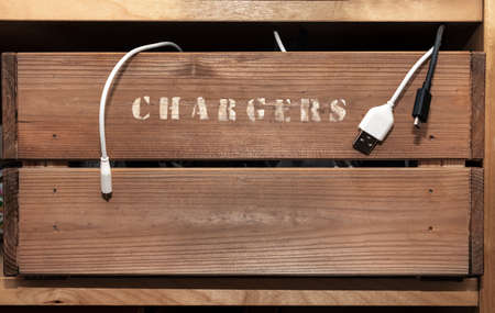 An old vintage style crate on a shelf with the word chargers hand painted on the side. Cables hang...