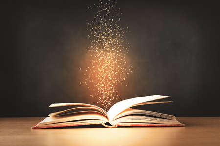 An old, worn, red text book, lying opened on a classroom desk with sparkles and stars rising upwards...