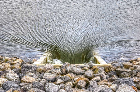 Strong current in a river towards a culvert in a dikeの写真素材
