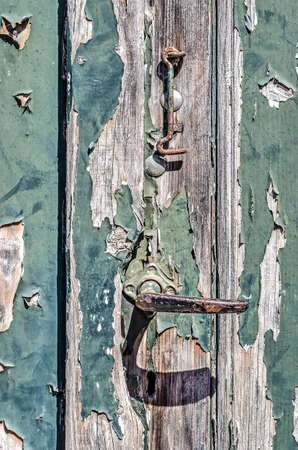 Close-up of a rusty steel door knob and hook on a weathered wooden door with peeling reen paintの写真素材