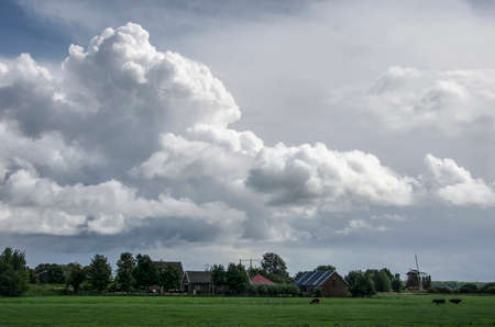 Dramatic cloudscape over a polder landscape with grassland, a farm and a windmill near Nigtevecht, The Netherlandsのeditorial素材