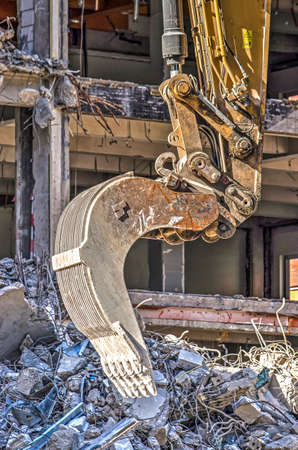 Close-up of an excavator at a demolition site, with the partially demolished building in the backgroundの写真素材
