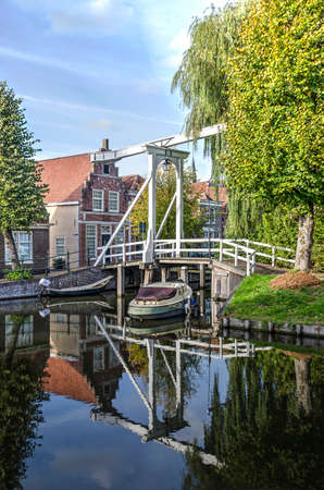 Monnickendam, The Netherlands, October 7, 2018: white wooden pedestrian drawbridge, canal houses and trees reflecting in a canal in the old townのeditorial素材