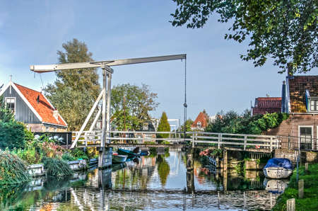 Edam, The Netherlands, October 7, 2018: white wooden drawbridge across a canal with houses, trees and gardens on both sidesのeditorial素材