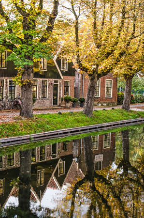 Edam, The Netherlands, October 7, 2018: canal houses with wooden and brick facades and trees in autumn colors reflecting in the calm water of the IJe canalのeditorial素材