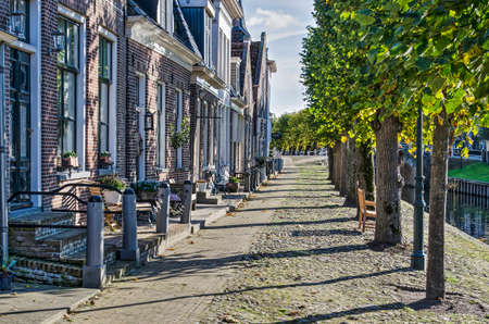 Sloten, The Netherlands, October 28, 2018: row of houses and line of trees on the cobblestone-paved quay of the main canalのeditorial素材