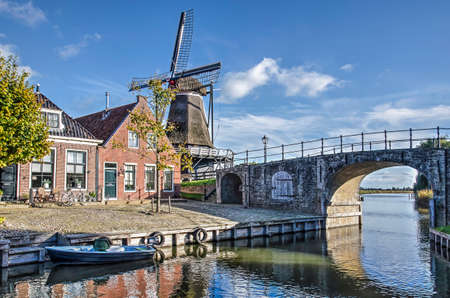 Sloten, The Netherlands, October 28, 2018: view of the main canal, houses and a windmill and, underneath a stone bridge, towards the open landscape just outside of the townのeditorial素材