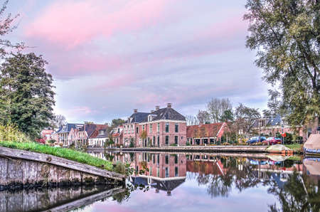 Leeuwarden, The Netherlands, November 3, 2018: Old houses in the neighbourhood of Snakkerburen reflect in the calm water of Dokkumer Ee canal under a purple sky at sunsetのeditorial素材