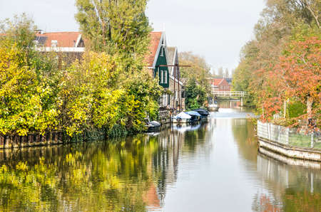 Bolsward, The Netherlands, November 4, 2018: Houses with sloops moored in front and gardens with trees and bushes next to a canal just outside the historic town centerのeditorial素材