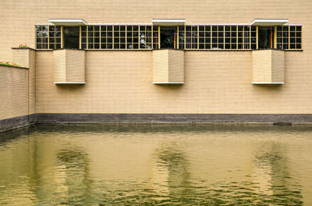 Hilversum, The Netherlands, September 20, 2018: detail of the south facade of the city hall by architect W.M. Dudok (1931) with a window and tree balconies reflecting in the adjacent pondのeditorial素材