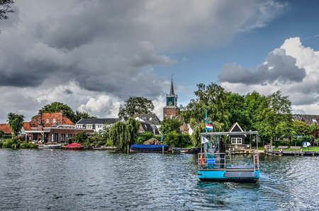 Nigtevecht, The Netherlands, August 25, 2018: small pedestrian ferry boat crossing the river Vecht under a dramatic skyのeditorial素材