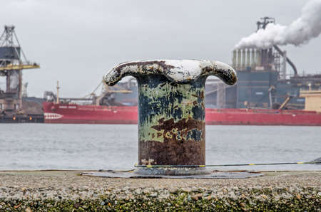 IJmuiden, The Netherlands, December 22, 2018: steel mooring bollard at a concrete quay, with the Tata steelworks and the Northsea Canal in the backgroundのeditorial素材