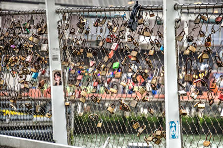 Rotterdam, The Netherlands, November 25, 2018: steel mesh railing of Rijnhaven bridge with many colorful locks as well ad photos, with the Katendrecht quay blurred in the backgroundのeditorial素材