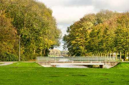 Nagele, The Netherlands, October 24, 2018: View from the central green area along a canal through an opening in the surrounding tree wall towards the open polder landscapeのeditorial素材