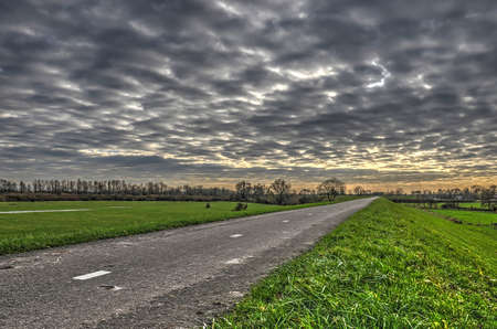 Asphalt road on a dike near Zaltbommel, The Netherlands under a dramatic skyのeditorial素材