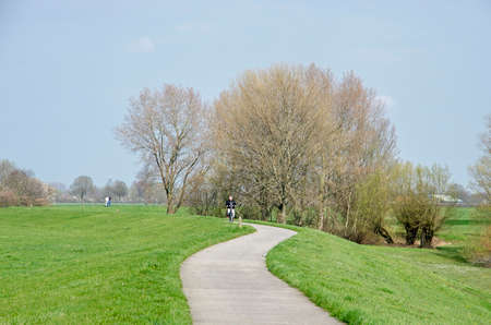 Doesburg, The Netherlands, March 30, 2019: hikers and a bicyclist on a narrow concrete path on a dike along the IJssel river on a sunny day in springtimeのeditorial素材