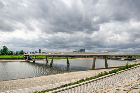 Nijmegen, The Netherlands, April 25, 2019: View from the stone-paved Lentse Warande river bank towards Lentloper bridge across the new channel of the river Waal under a dramatic skyのeditorial素材