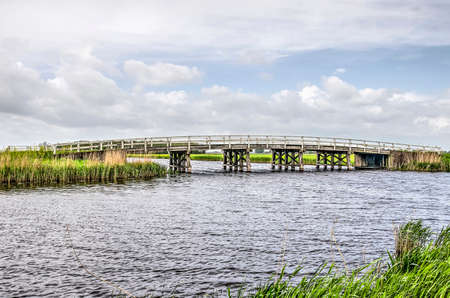 Junction of two canals in Alblasserwaard polder in the Netherlands with a wooden bridge on a windy...